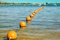 View of the sea from a shore with a long line of orange colored marker buoys floating