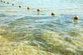 View of the sea from a shore with a long line of orange colored marker buoys floating