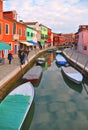 Burano island picturesque street with small colored houses in row, water canal with fishermans boats, cloudy blue sky Royalty Free Stock Photo