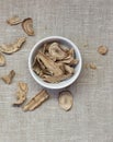 Burdock herb dried roots in a bowl flat from above on linen textile, overhead top view of wheat-grass Royalty Free Stock Photo