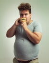 This burger is all mine. Studio shot of an overweight man biting into a burger.