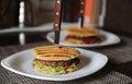 Burger with beef chops, guacamole, cherry sauce, potato bun on the grill. Stabbed with a knife with a wooden handle Royalty Free Stock Photo