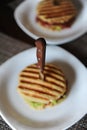 Burger with beef chops, guacamole, cherry sauce, stabbed with knife with wooden handle. Focus on the handle Royalty Free Stock Photo