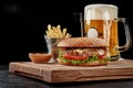 Burger with beef patty, blue cheese, caramelized onion, fresh vegetables served with pale lager, fries and sauce Royalty Free Stock Photo