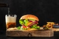 Burger and beer. Hamburger with beef, cheese, onion, tomato, and green salad, a side view on a dark background with copy space, Royalty Free Stock Photo