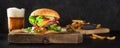 Burger and beer panorama. Hamburger with beef, cheese, onion, tomato, and green salad, with pickles and French fries, a Royalty Free Stock Photo