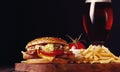 Burger with chicken cutlet, fried bacon and vegetables, French fries, glass of beer, on a wooden board, no people Royalty Free Stock Photo