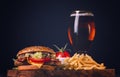 Burger with chicken cutlet, fried bacon and vegetables, French fries, glass of beer, on a wooden board, no people Royalty Free Stock Photo