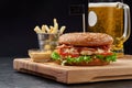 Burger with chicken patty, fried bacon, parmesan and vegetables served with beer, fries and aioli Royalty Free Stock Photo