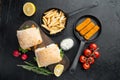 Burger with fish fingers fresh lettuce, tomato and tartar sauce, on wooden cutting board, on black background, top view flat lay Royalty Free Stock Photo