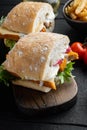 Burger with fish fingers fresh lettuce, tomato and tartar sauce, on wooden cutting board, on black wooden table background Royalty Free Stock Photo