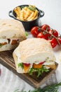 Burger with fish fingers fresh lettuce, tomato and tartar sauce, on wooden cutting board, on white background Royalty Free Stock Photo