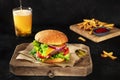 Burger with French fries and beer. Hamburger with beef, cheese, onion, tomato, and green salad, on a dark background Royalty Free Stock Photo