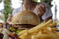 Burger and French fries closeup photo with eating woman on background. Restaurant lunch with beef burger.