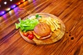 Burger with French fries on a round board on a wooden table with multicolored lights on the background Royalty Free Stock Photo