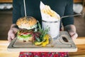 Burger with fries and vegetables on a board in hand. Dinner main dish on a wooden table. Traditional polish cuisine