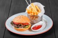Burger, hamburger with french fries, ketchup, mayonnaise, fresh vegetables and cheese on plate on dark wooden background. Royalty Free Stock Photo