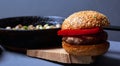 Burger with a juicy cutlet tender bun and champignon mushrooms in a castiron pan on a wooden rustic plate on a gray background.