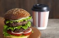 Burger with paper coffee cup to go on wooden tabletop. Close up Royalty Free Stock Photo