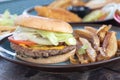 burger with toasted beef lettuce tomatoes onions and cheese next to fried potatoes on a plate Royalty Free Stock Photo