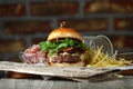 Burger on the wooden table with cheese, bacon, tomatos, green and red salad and french fries