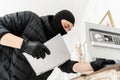 Thief with black balaclava stealing modern Electronic safe box. The burglar commits a crime in Luxury apartment with