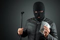 Burglar, a thug in a balaclava holds dollars in his hands on a dark background. Robbery, hacker, crime, theft. Copy space