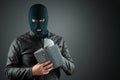 Burglar, a thug in a balaclava holds dollars in his hands on a dark background. Robbery, hacker, crime, theft. Copy space