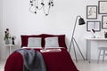 Burgundy bedding and gray pillows on a bed in a white wall bedroom interior. Real photo. Royalty Free Stock Photo