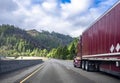 Burgundy big rig classic semi truck with dry van semi trailer running on the winding mountain highway road Royalty Free Stock Photo