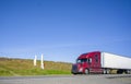 Burgundy bonnet big rig semi truck transporting cargo in dry van semi trailer driving on the road with hillside Royalty Free Stock Photo