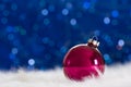 Burgundy Christmas ball on white fur with garland lights on blue