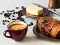 Burgundy color coffee cup with espresso with croissant. In the background are fresh coffee beans, butter and cezve. Located on a Royalty Free Stock Photo