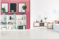 Burgundy wall with gallery of graphics and bookshelf in tasteful bedroom interior