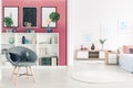 Burgundy wall with posters and bookshelf in contemporary bedroom interior with grey chair