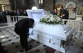 Burial service in a church: man dressed in black mourning costume kissing the late lying in the white coffin