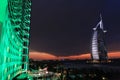 Burj Al Arab at night, Luxury 7 Stars Hotel Beautiful Building. Corner view of Jumeirah Beach Hotel in green lighting. Cloudy sky