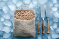 Burlap sack filled with raw nuts sits on ice, accompanied by three stainless steel kitchen tools, creating a fresh and inviting Royalty Free Stock Photo