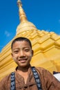 Burmese child with traditional Thanaka face paint poses in front of gold stupa.