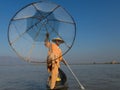 Burmese fisherman leaning on oar posing in traditional clothes with hand and foot holding his cone shaped fishing net