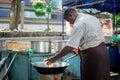 A burmese man in traditional longyi fries an egg in a wok pan