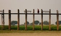 Burmese monk in red clothes walking on Ubein Bridge