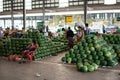 A burmese woman carries a heavy bag on her head next to huge piles of fresh watermelons at a local street market Royalty Free Stock Photo