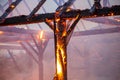 Burned down wooden barn with fire and sparks still blazing. Charred roof truss and wooden posts