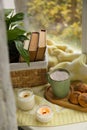 Burning aromatic candles, cup with hot drink and cookies on windowsill indoors. Autumn coziness Royalty Free Stock Photo