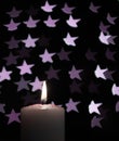 Burning candle with blur violet stars on black background