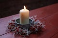 Burning candle in a bowl decorated with a small wreath from rose hips and silver cushion bush on a red wooden table, winter Royalty Free Stock Photo