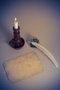 Burning candle in candlestick, letter paper blank, quill pen, inkwell on the table. Vintage style filtered photo Royalty Free Stock Photo