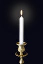 Burning candle in figured gilded candlestick in darkness
