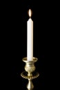 Burning candle in figured gilded candlestick, isolated on black background.